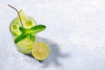 One glass with iced green matcha tea with lime, ice, fresh mint and metal drinking straw on light grey backdrop with trendy shadows. Healthy food, No Plastic, Zero Waste concepts. Copy space for text.