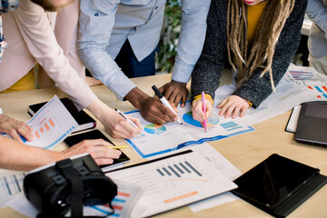 Cropped close up image of multiethnic diverse business team analyzing income charts and graphs with...