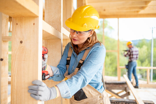 Female worker at construction site during work with wood frame house