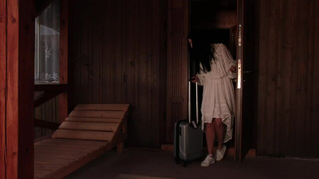 Rear view of a beautiful slim young brunette woman with suitcase leaves hotel room after long therapeutic vacation. Female goes on business trip leaving house, luggage, tourism, departure, fees travel