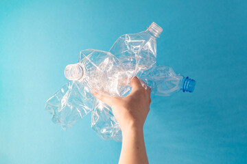Recycling concept. Female hand holds a rumpled plastic bottles. Ecological problem, top view, blue background.