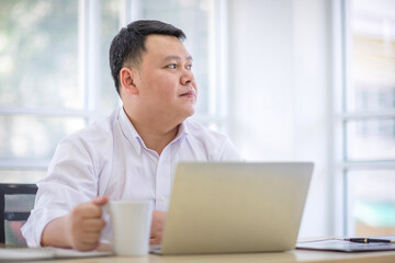 Asian Men Wearing a white shirt holding a white coffee cup. Relaxing and drinking coffee in office