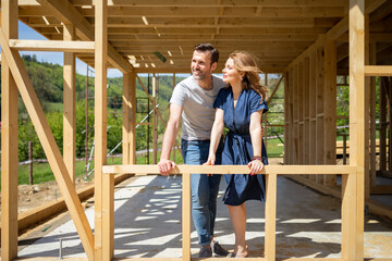 Couple standing on future window in construction site of their new house, dreams come true