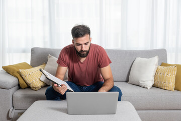 Young freelancer worker man typing the new business contract and plan in his laptop from printed notes to send it through mail to his boss