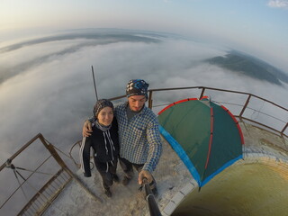 Camping on top of a smoke stack chimney, surrounded by fog and mist underneath the top of the building, sunrise