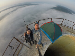 Camping on top of a smoke stack chimney, surrounded by fog and mist underneath the top of the building, sunrise