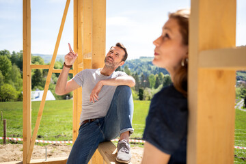 Obraz premium Couple sitting on frame of window in construction site of their new house planning future together