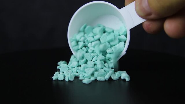 Granules are poured from a measuring spoon on a black background