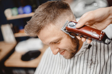 Barber in Barbershop shear hair electric to young guy for fashionable hairstyle