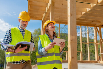 Construction engineer and architect consult plans on building site of wood framing house under...
