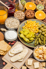 Canned cucumbers, corn, pepper in a ceramic plate. Sausages in pan. Chickpeas olives, tomatoes.