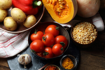 Vegetables and spices on an old table: potatoes, bell pepper, pumpkin, tomatoes, garlic, dried peas, turmeric, smoked paprika and chili flakes