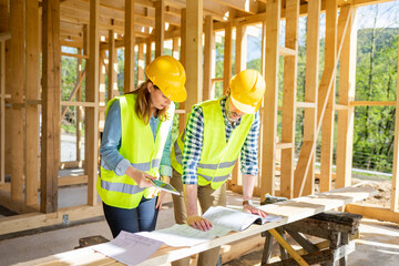 Construction engineer and architect consult plans on building site of wood framing house under...