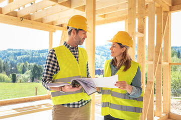 Construction engineer and architect consult plans on building site of wood framing house under...