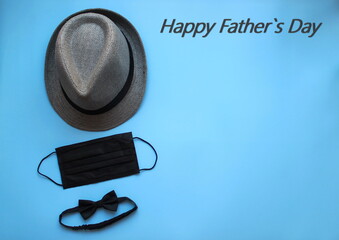 Happy Father's Day greeting text. Men's hat, bow tie, sunglasses, black face mask on a blue background. The concept of father's Day during the coronavirus. Flat Lay