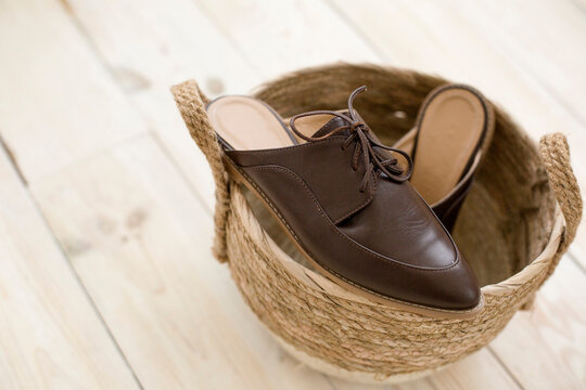 brown leather shoes for women without a heel lie in a wicker basket of straw. Trending photo of spring autumn footwear. elegant flip flops.shoelaces
