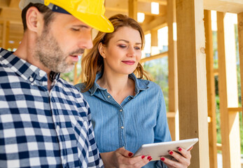 Architect or engineer with blueprints meeting with owner of building house on construction site