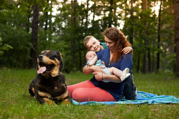 Fototapeta premium Mom relaxing on blanket with baby and son and big dog in the forest