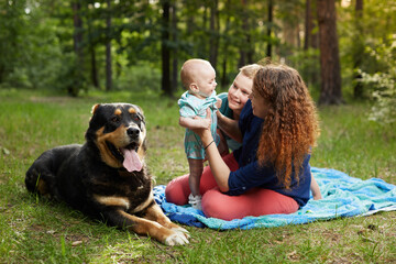 Mom relaxing on blanket with baby and son and big dog in the forest