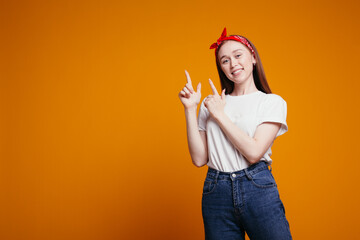 Redhead girl in a red bandana points fingers up and smiles while looking at the camera. Emotional...