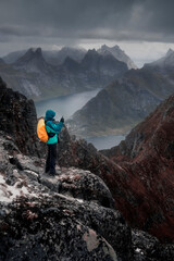 Mount Munken to fjord under a stormy sky at sunset on the Lofoten Islands, Polar, Norway,  a man stands on top and takes a photo on his mobile phone