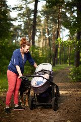 Adult caucasian woman with her baby in baby carriage in forest