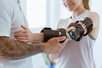 Tattooed physiotherapist who puts an orthosis on the hand of a young patient after an accident