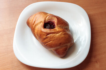 tasty baked bun with crispy golden crust and sweet berry jam on a white plate on a wooden table. sweet snack