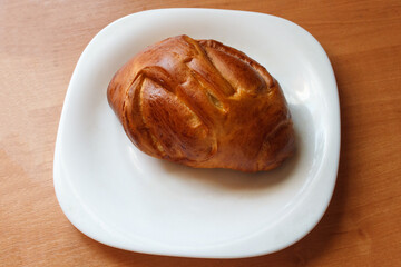 tasty baked bun with crispy golden crust and sweet berry jam on a white plate on a wooden table. sweet snack