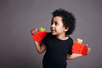 Close-up portrait of African american boy in a black T-shirt holding red skateboard behind his back...
