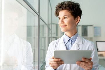 Smiling attractive laboratory worker with curly hair satisfied with research results using digital tablet