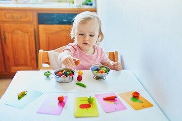 Adorable little girl playing with toy fruits and vegetables at home