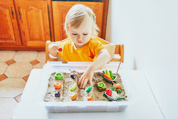 Adorable little girl playing with toy fruits and vegetables and kinetic sand at home