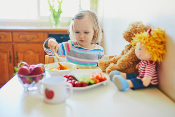 Adorable toddler girl eating fresh fruits and vegetables for lunch
