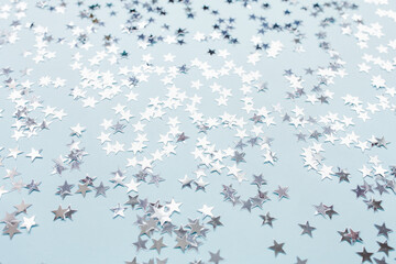 Trendy silver foil confetti stars on light blue background. Christmas festive abstract backround....