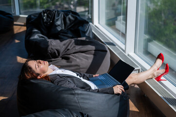 Business lady sleeps sitting in a modern office comfortable bob chair bag. A woman in a suit fell asleep at work on a laptop. Caring for the convenience and comfort of employees.