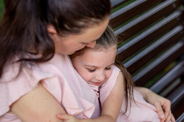 mother and daughter 5-6 years old walk in the Park in the summer, mother hugs her daughter sitting on a bench, the concept of a happy family, the relationship of mother and child, mother's day