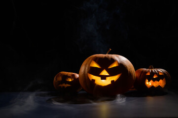 Three creepy halloween steaming pumpkins with a carved luminous smirk on a black background. A...