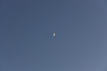 The yellow small growing moon on the blue sky
