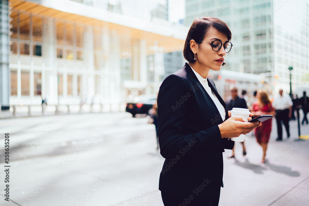 Poster side view of businesswoman in eyewear reading received notification on smartphone while standing on 