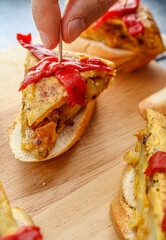 Spanish tortilla pintxo on a wooden board. Potato omelette on bread as a basque canape on sharing board. Party food. 