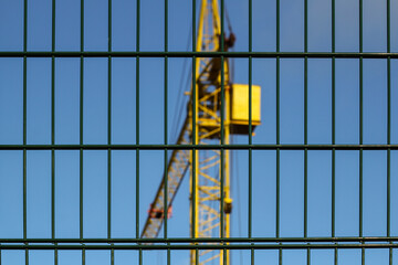 Yellow construction crane on construction site with fence in foreground and lots of blue sky
