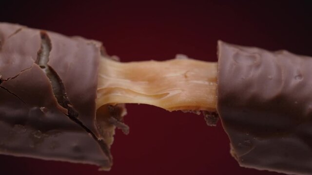 Close-up slow motion footage of soft caramel stretching and separating between two layers of milk chocolate. Gooey caramel texture pulls apart in a smooth, elastic motion, revealing glossy melted choc