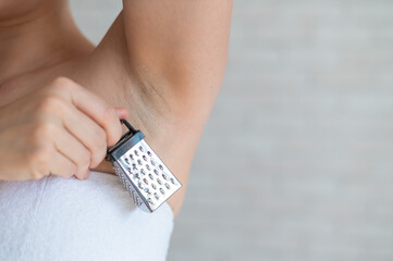 Unrecognizable woman in a white terry towel holds a mini grater depicting shaving irritations....