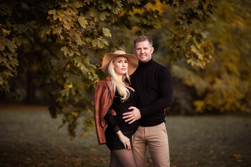 Young blond pregnant woman posing with man at the autumn background. Copy space.