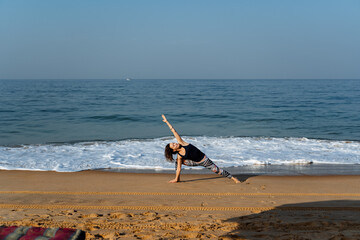 Fototapeta na wymiar a young girl of European appearance does yoga on the beach early in the morning, practicing asana on the beach in India