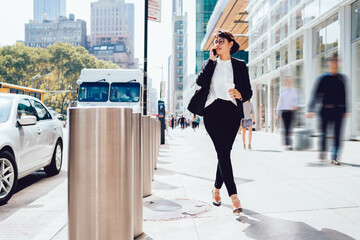 Confident woman in spectacles dressed in elegant suit strolling around modern streets in New York...