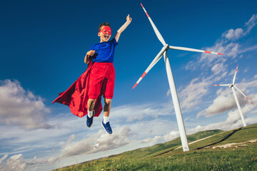 Superhero kid is in front of the wind farm. Little child plays superhero.