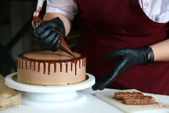 confectioner process chocolate cake on table. The process of decorating the cake with liquid chocolate. The process of making the chocolate cake on dark background
