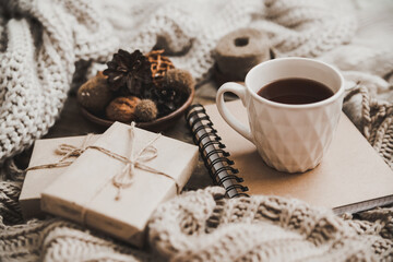 Sweaters and cup of tea with notebook, candle and knitting clothes. Cozy autumn or winter concept.